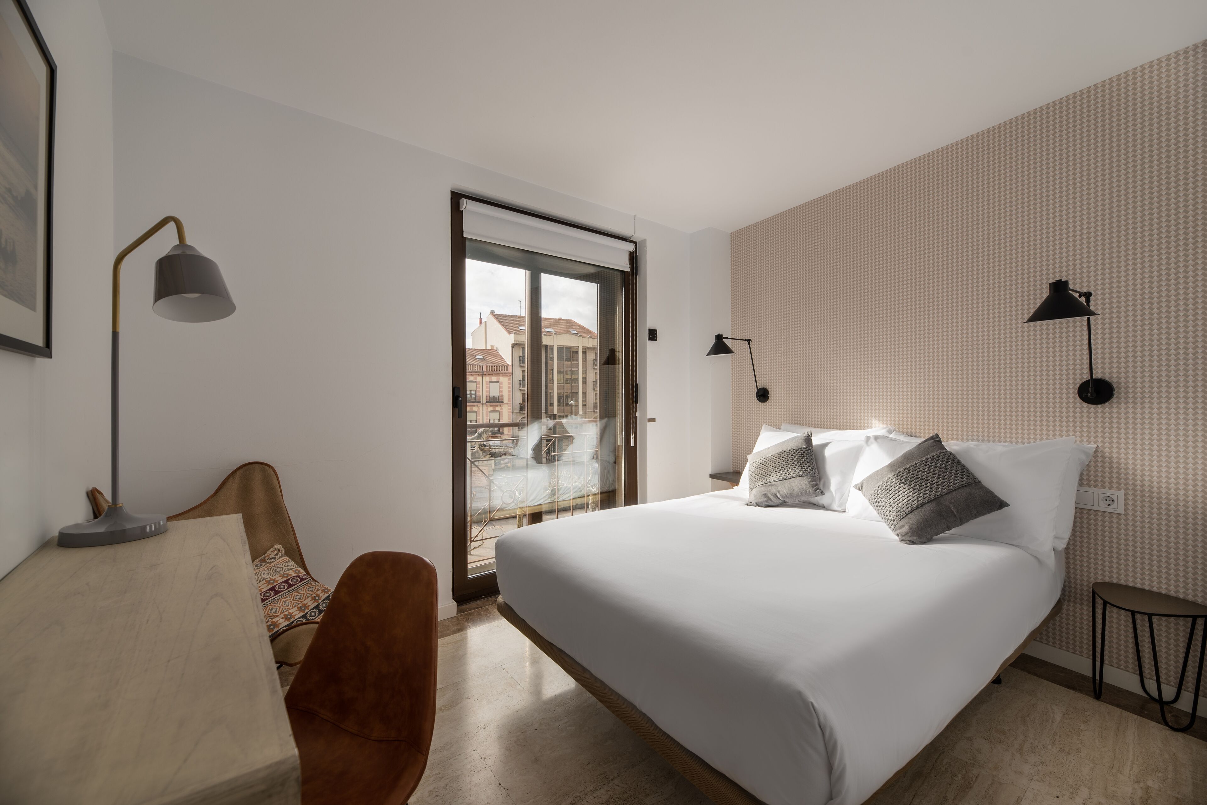 A hotel room with a bed, a chair, a desk, and a view of the outside.