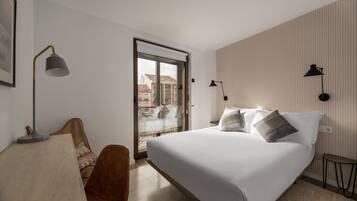 A hotel room with a bed, a chair, a desk, and a view of the outside.