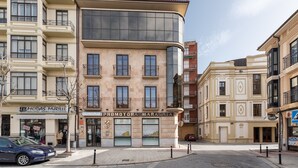 Un edificio de varios pisos con una fachada curva de vidrio destacada, una entrada a nivel de la calle y varios balcones.