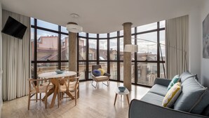 Un salón moderno con una mesa redonda de comedor, un sofá gris y un amplio ventanal con vistas a la ciudad.