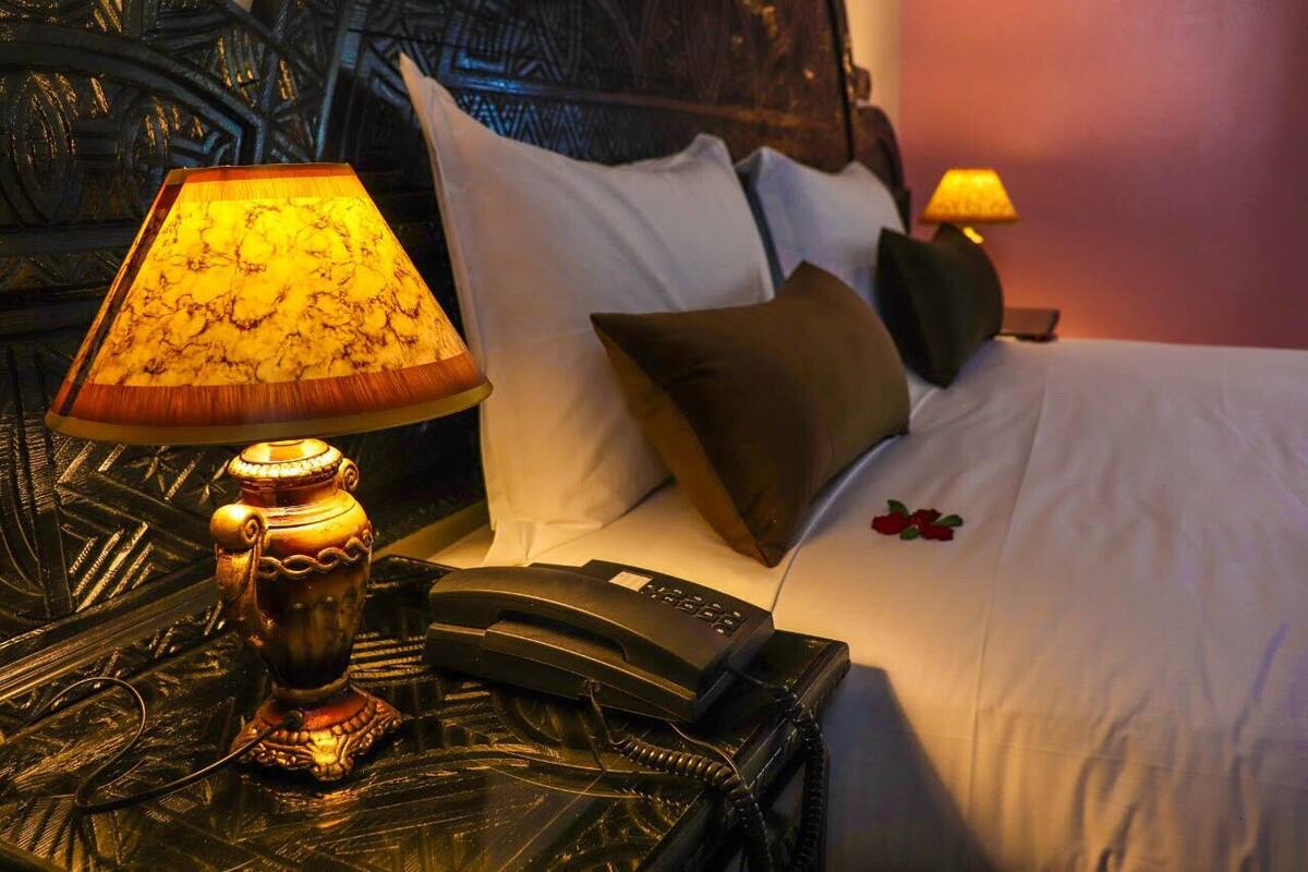 A hotel room with a bed, pillows, a bedside lamp, a telephone, and a decorative wall headboard.