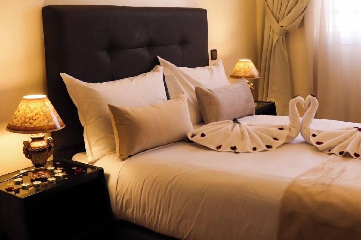 A neatly made bed with white linens, a dark headboard, and decorative swan-shaped towels.