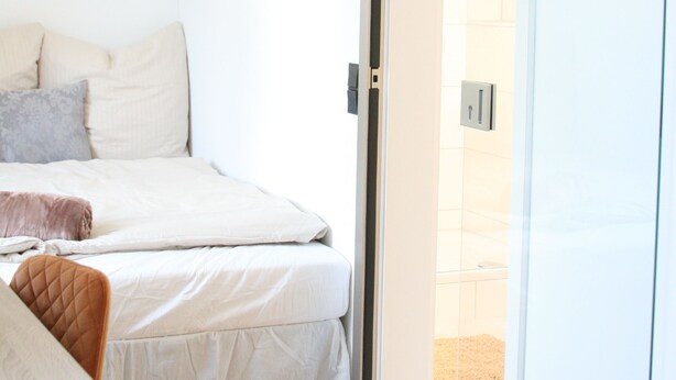 A bedroom with a bed, a chair, and a sliding glass door leading to a bathroom. - The Manhattan A Boutique Hotel By American Ease (Grafenwohr)