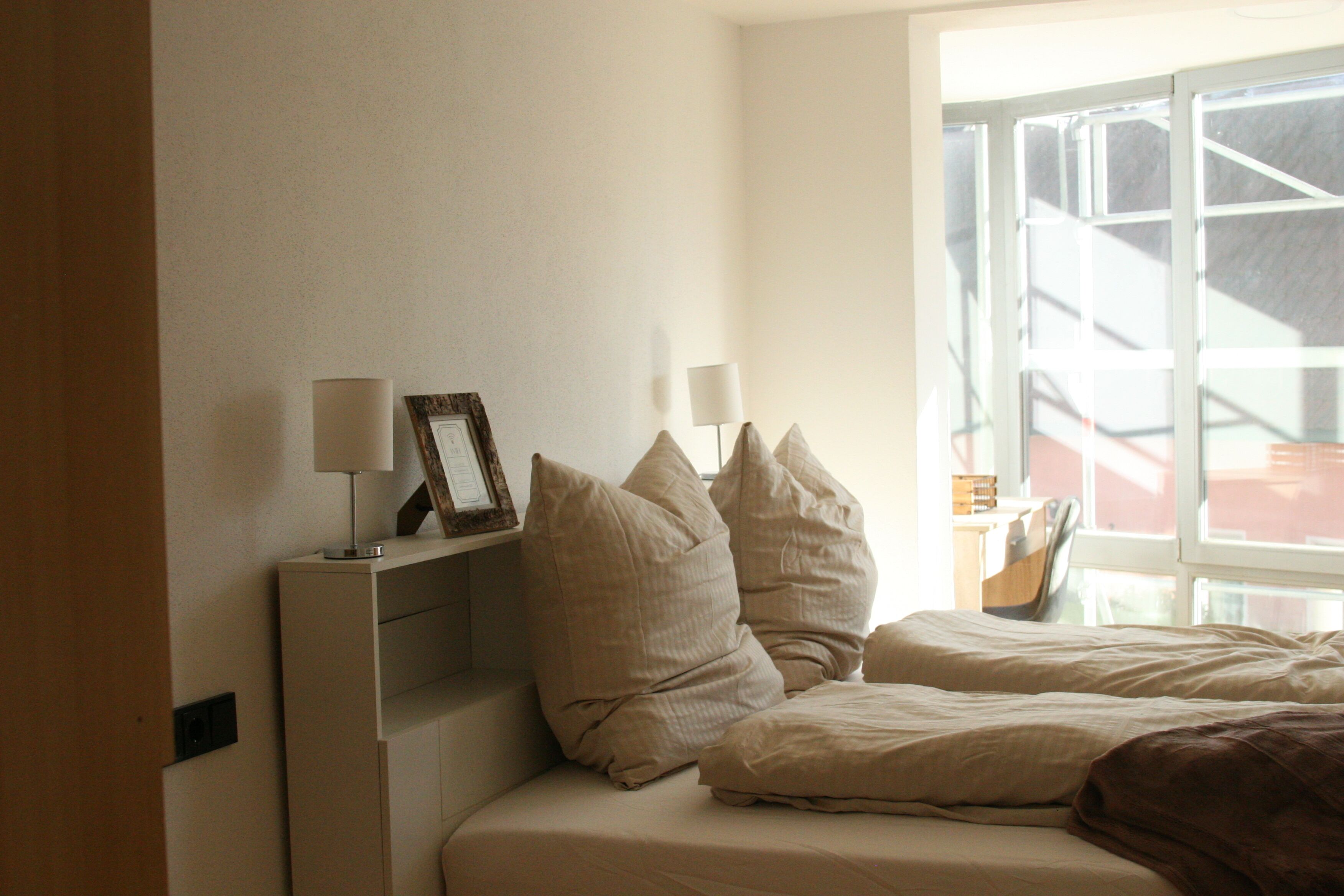 A bedroom with a bed, pillows, a bedside table, and a lamp.