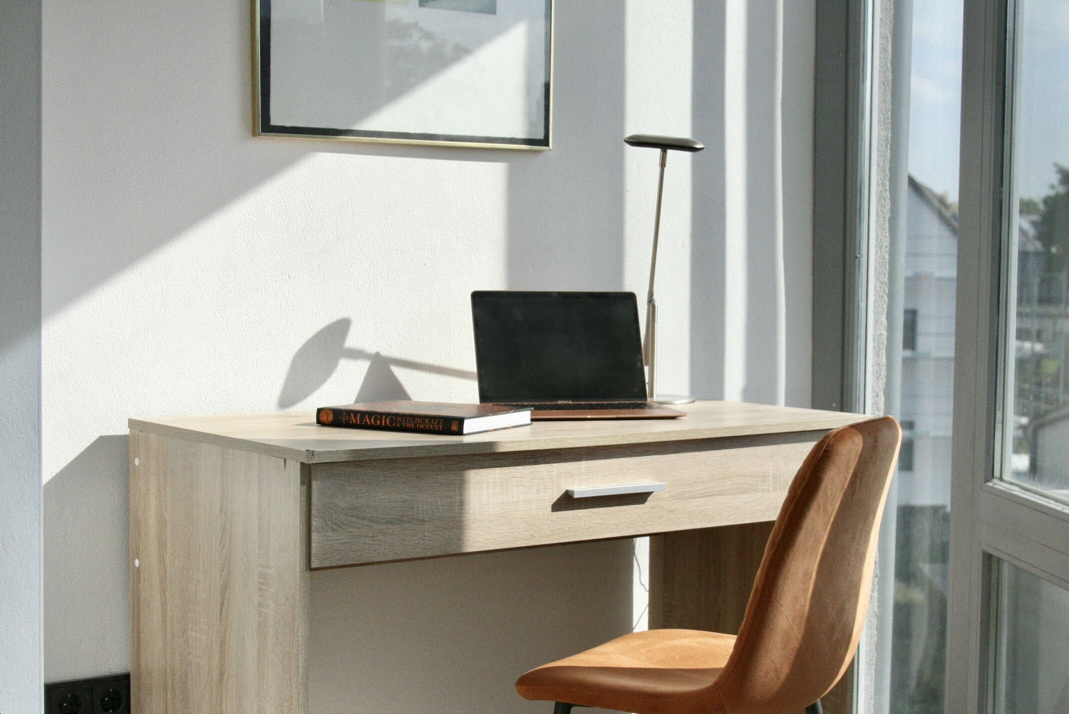 A wooden desk with a laptop, a book, and a lamp.