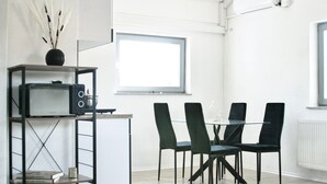 A modern dining area with a table and four chairs, a small kitchenette with a microwave, and a window providing natural light. - The Manhattan A Boutique Hotel By American Ease (Grafenwohr)