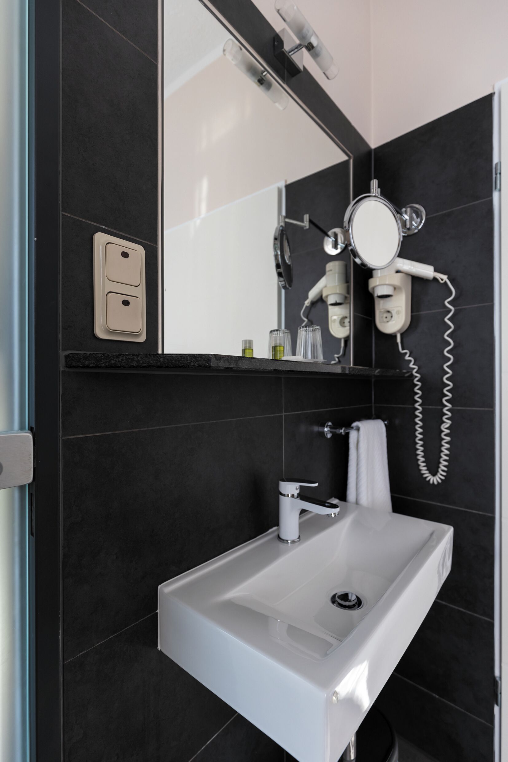 Ein modernes Badezimmer mit einem weißen Waschbecken, einem Spiegel und einem an der Wand befestigten Fön.