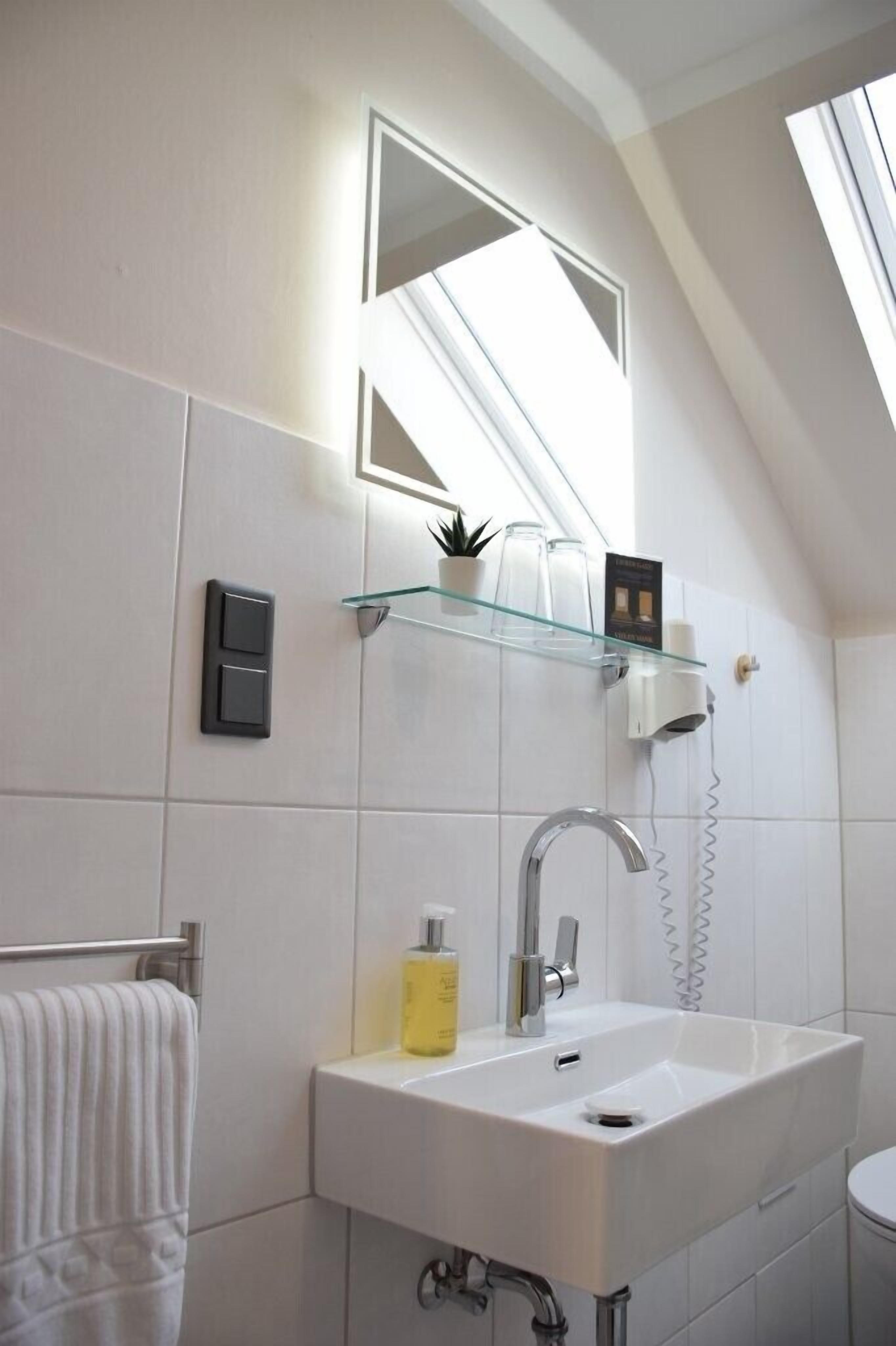 A modern bathroom with a skylight, a white sink, a glass shelf with toiletries, and a towel rack.