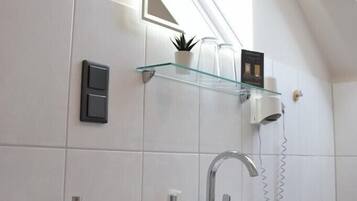 A modern bathroom with a skylight, a white sink, a glass shelf with toiletries, and a towel rack.