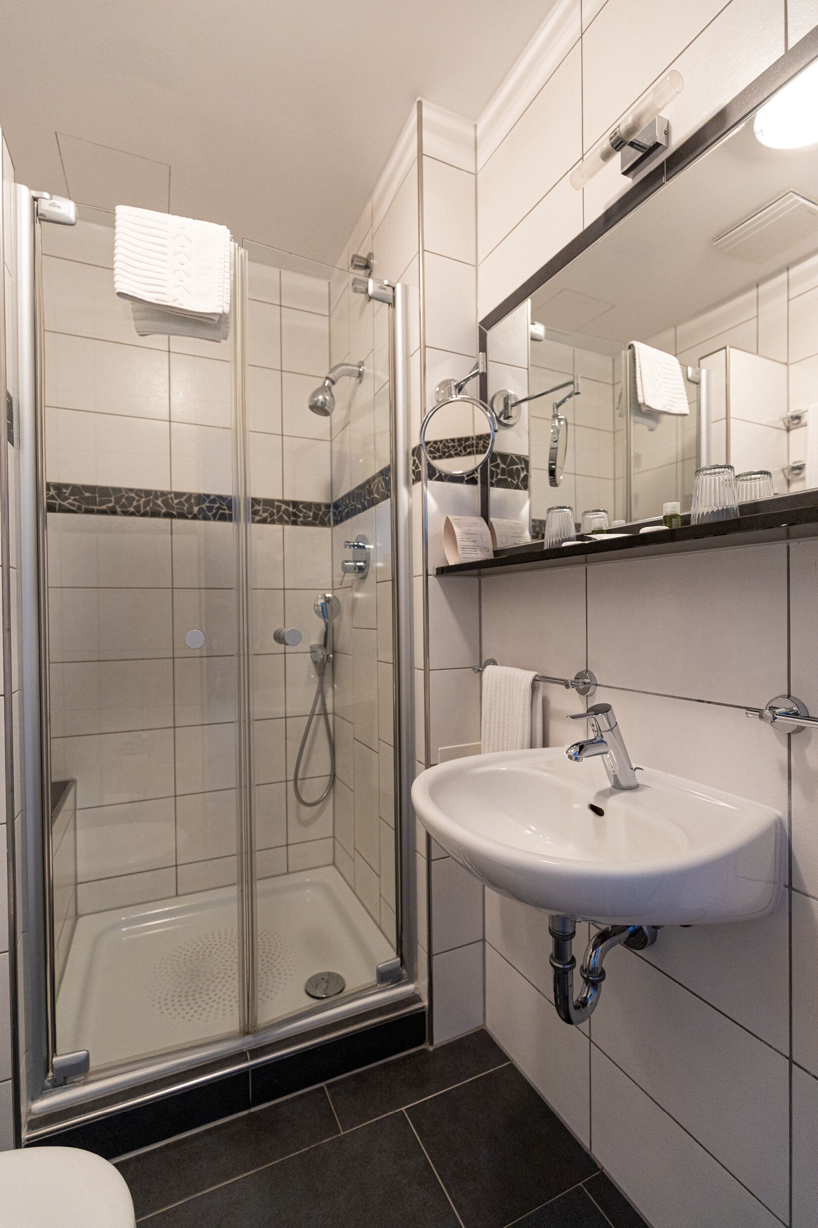 Een moderne badkamer met een douchecabine van glas, een witte wastafel en een spiegel erboven.