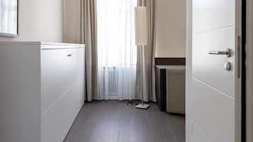 Una habitación de hotel con piso de madera, una cama, un armario, un escritorio y una ventana con cortinas.