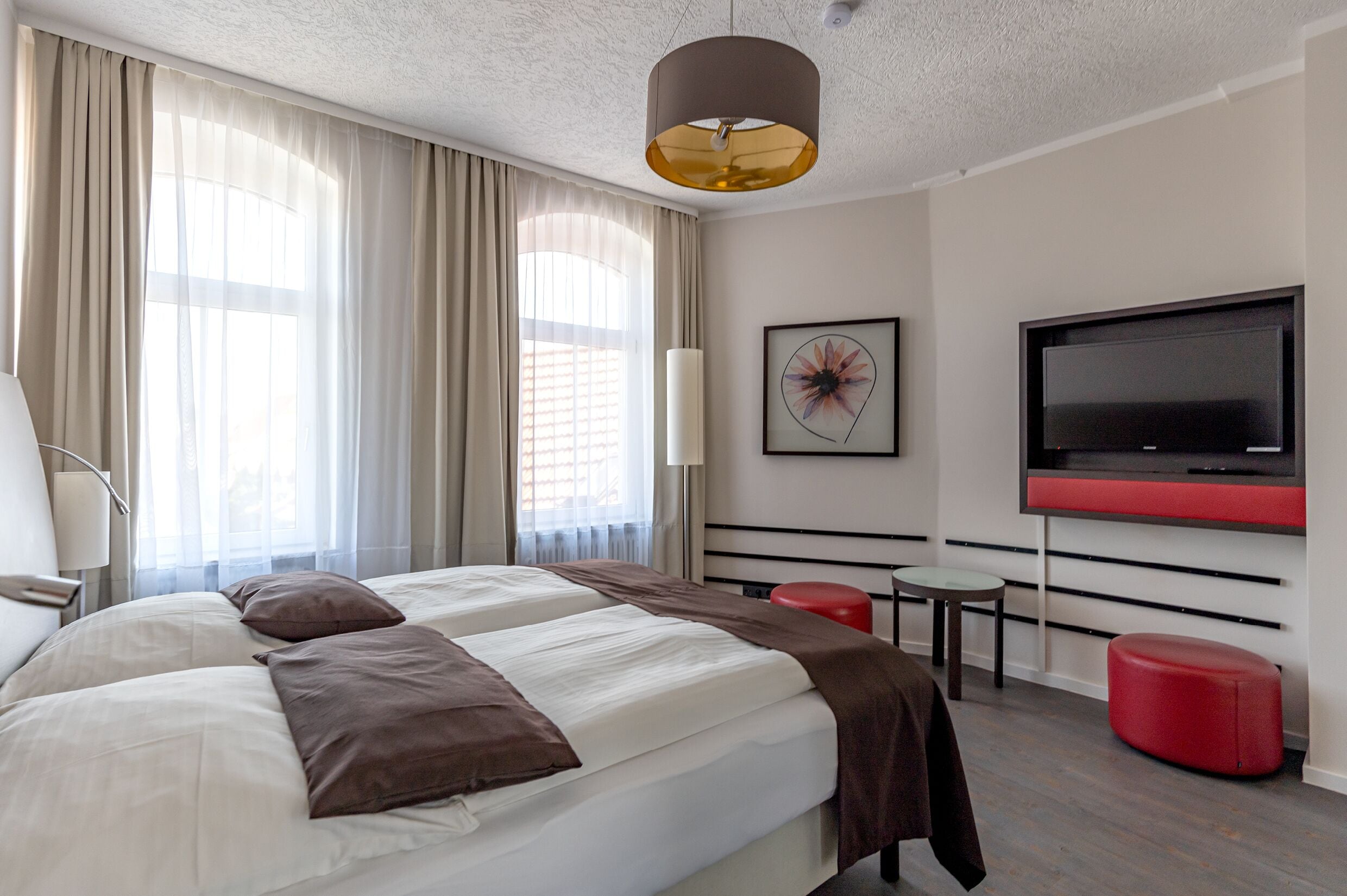Una habitación de hotel moderna con una cama grande, un televisor, un reposapiés rojo y una pequeña mesa.