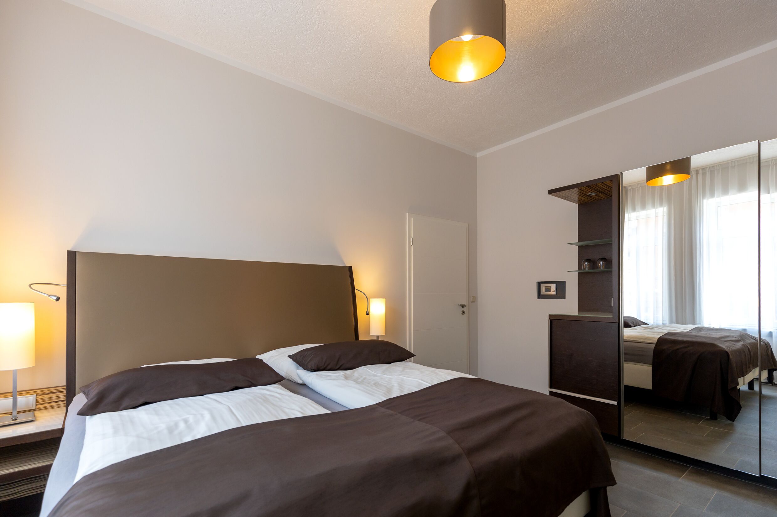 Una habitación de hotel con una cama grande, una lámpara de noche, un espejo y un armario.
