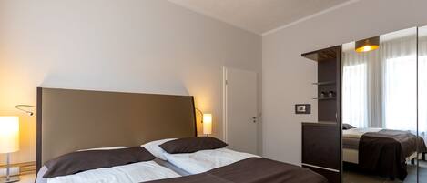 Una habitación de hotel con una cama grande, una lámpara de noche, un espejo y un armario.