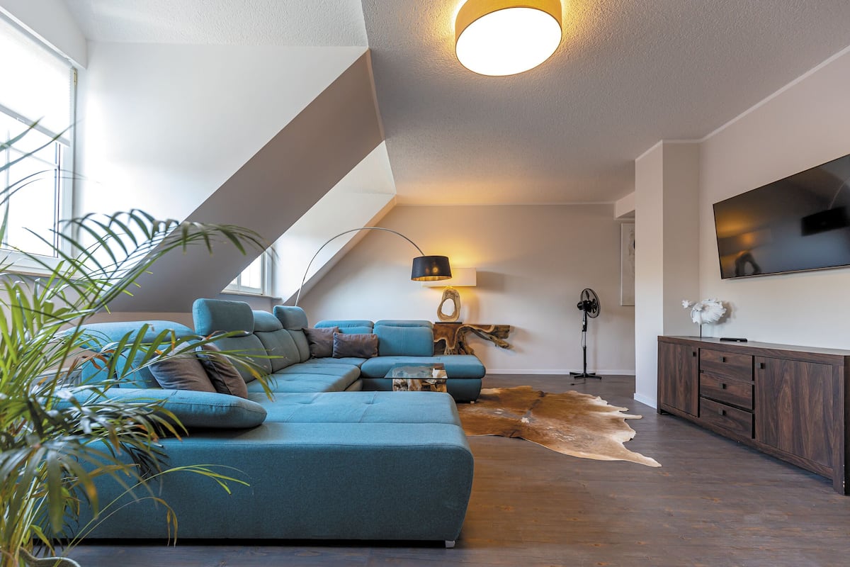 A modern living room with a sectional sofa, a flat-screen TV, and a ceiling fan.