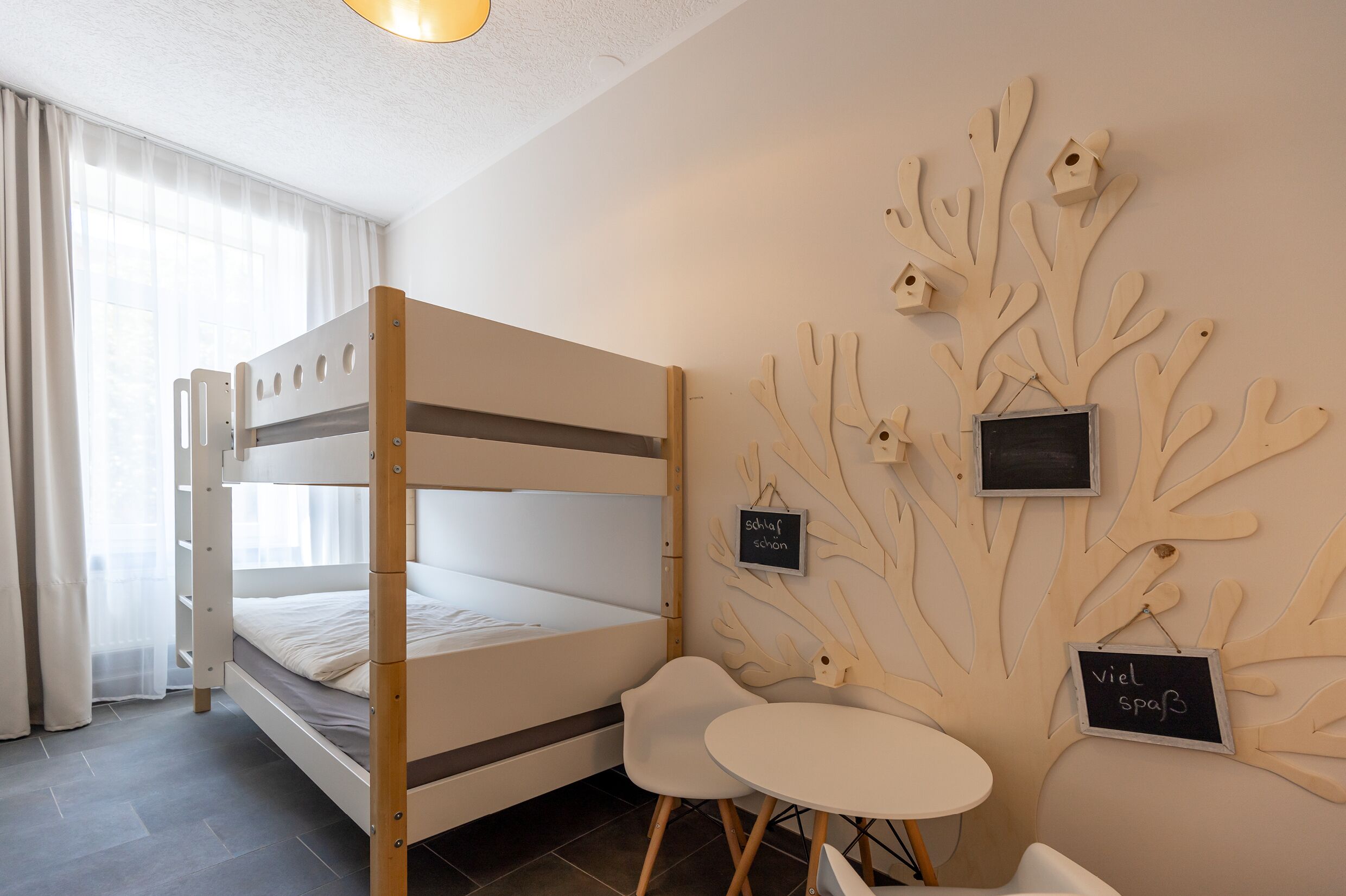 Ein Etagenbett mit einem kleinen Tisch und Stühlen, eine Wand mit Holzzweigen und Vogelhäusern, sowie ein Schild mit Text.