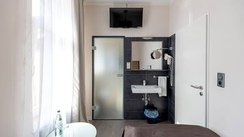 Habitación de hotel moderna con cama, una mesa redonda, una botella, un lavamanos blanco y zona de ducha.