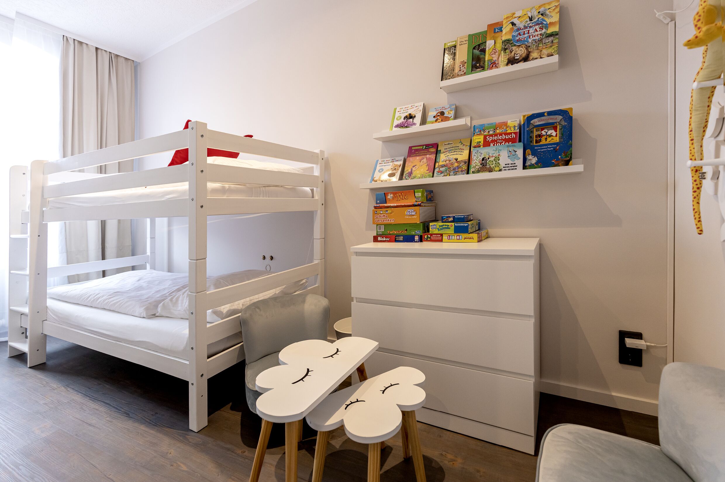 A bunk bed with a desk and chair, a bookshelf with children's books, and a small table with a teddy bear.