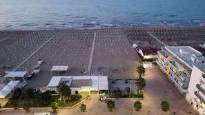 An aerial view of a beach with rows of umbrellas and a building with multiple floors and balconies. - Special Family Apartment 2 Steps From the sea (Margherita di Savoia)