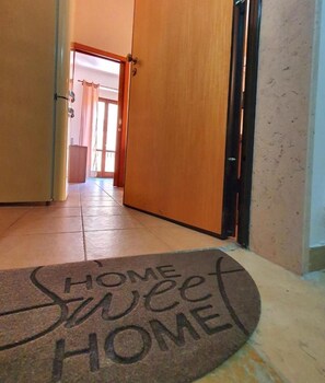 A hallway with a wooden door, a doormat with "HOME SWEET HOME" text, and a number "102" on the wall. - Special Family Apartment 2 Steps From the sea (Margherita di Savoia)