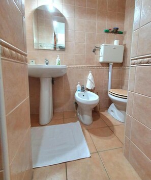 A small bathroom with beige tiles, a pedestal sink, a bidet, a toilet, and a mirror. - Special Family Apartment 2 Steps From the sea (Margherita di Savoia)