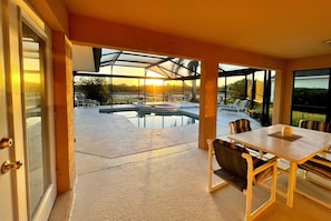 En täckt uteplats med en pool, utomhusmöbler och utsikt över solnedgången.