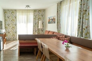 A living room with a sofa, a dining table, and a bench. There is a lamp on the table and a flower vase. - Easyapartments Riverside (Salzburg)