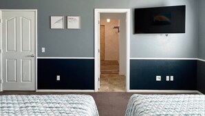 A bedroom with two beds, a TV mounted on the wall, and a door leading to another room. - Room in House - Cheerful And Cozy one Large Bedroom (Jurupa Valley)