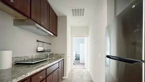 A kitchen with dark wooden cabinets, a stainless steel refrigerator, and a marble countertop. - Room in House - Cheerful And Cozy one Large Bedroom (Jurupa Valley)
