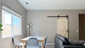 A modern living room with a dining table, two grey chairs, a grey sofa, and a wooden floor. - Room in House - Cheerful And Cozy one Large Bedroom (Jurupa Valley)