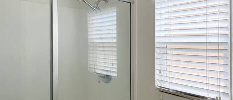 A glass-enclosed shower with a handheld showerhead, a glass door, and a window with blinds.