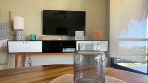 A living room with a wooden table, a glass jar, a TV, and a window. - Family Apartment in Beautiful Residential Complex in Holbox (Isla Holbox)