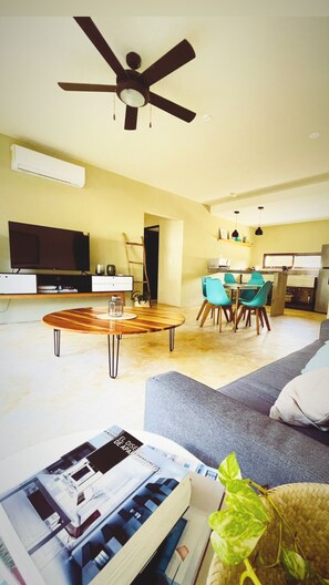 Ein Wohnzimmer mit Deckenventilator, Fernseher, Essbereich mit Stühlen und einer Couch.