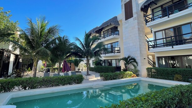 A poolside area with a pool, palm trees, and modern buildings with balconies. - Family Apartment in Beautiful Residential Complex in Holbox (Isla Holbox)