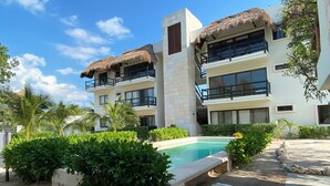 A resort with a pool, thatched-roof buildings, and lush greenery. - Family Apartment in Beautiful Residential Complex in Holbox (Isla Holbox)