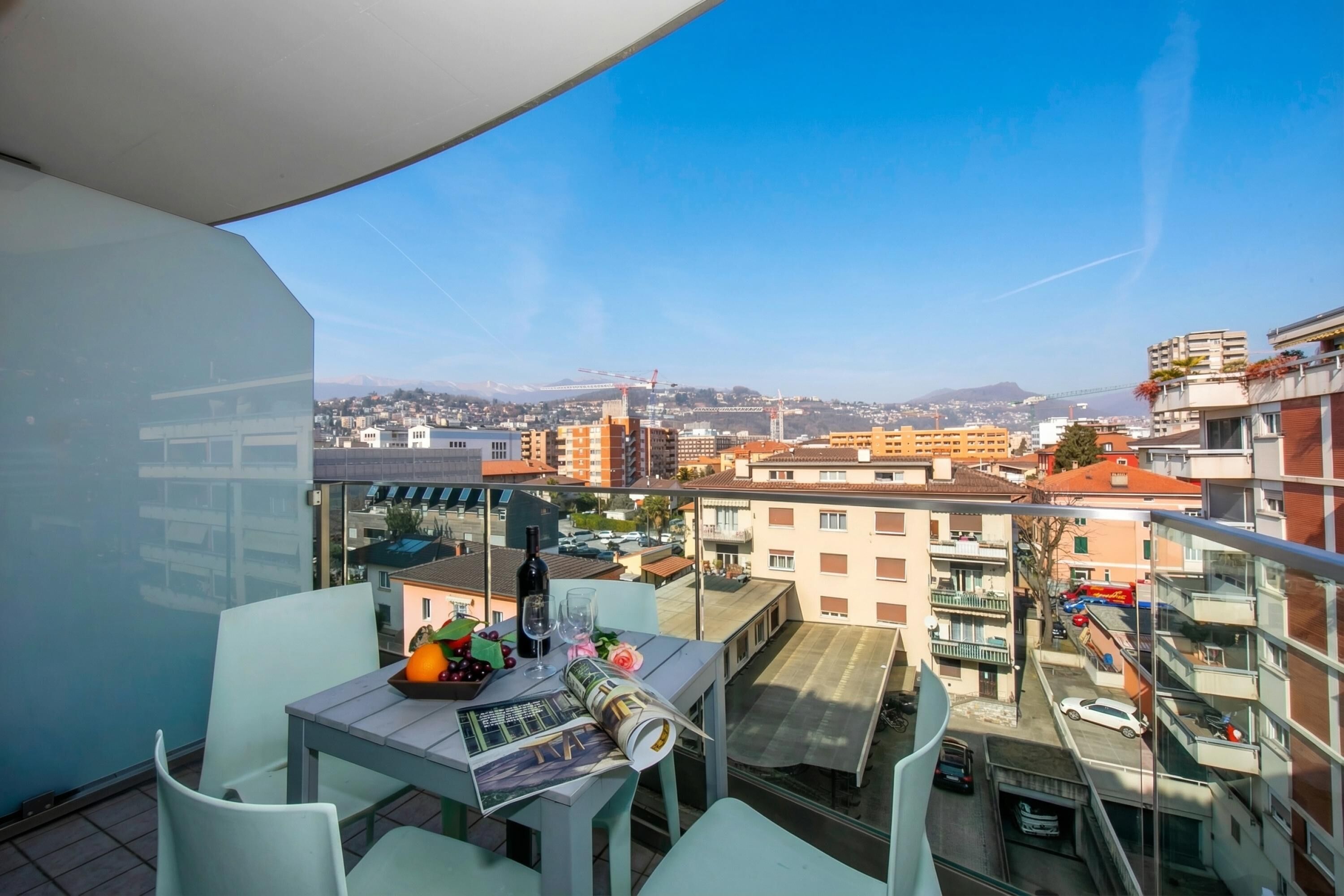 Un balcón con una mesa, sillas y vistas a un paisaje urbano con edificios y un puente.