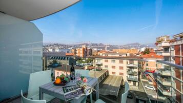 Un balcón con una mesa, sillas y vistas a un paisaje urbano con edificios y un puente.