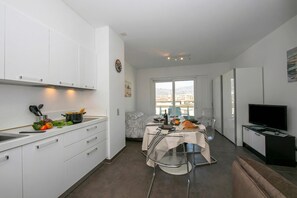A modern kitchen with white cabinets, a dining area with a table set for two, and a TV in the living area.
