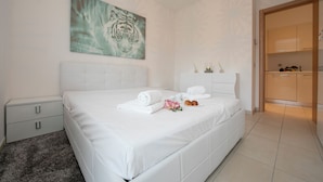 A modern bedroom with a large bed, a white headboard, a painting of a tiger, and a chandelier. - Via al Chioso Apartments (Lugano)