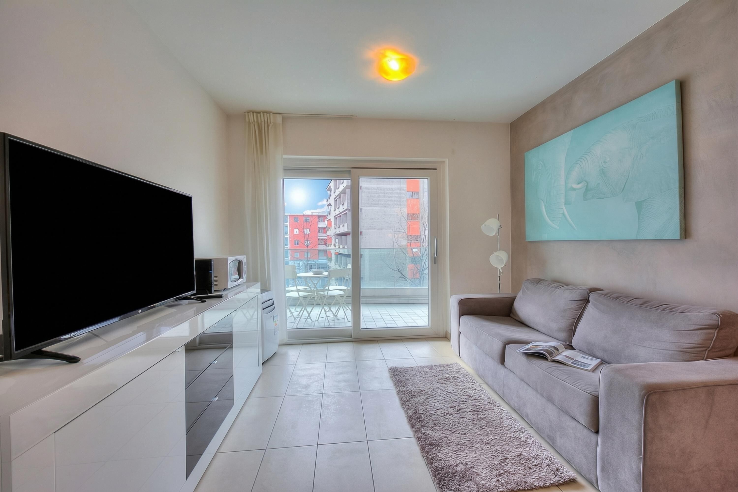 Una sala de estar moderna con un televisor de pantalla plana, un sofá, un cuadro y un ventanal corredizo que da a un espacio al aire libre.