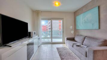 Una sala de estar moderna con un televisor de pantalla plana, un sofá, un cuadro y un ventanal corredizo que da a un espacio al aire libre.