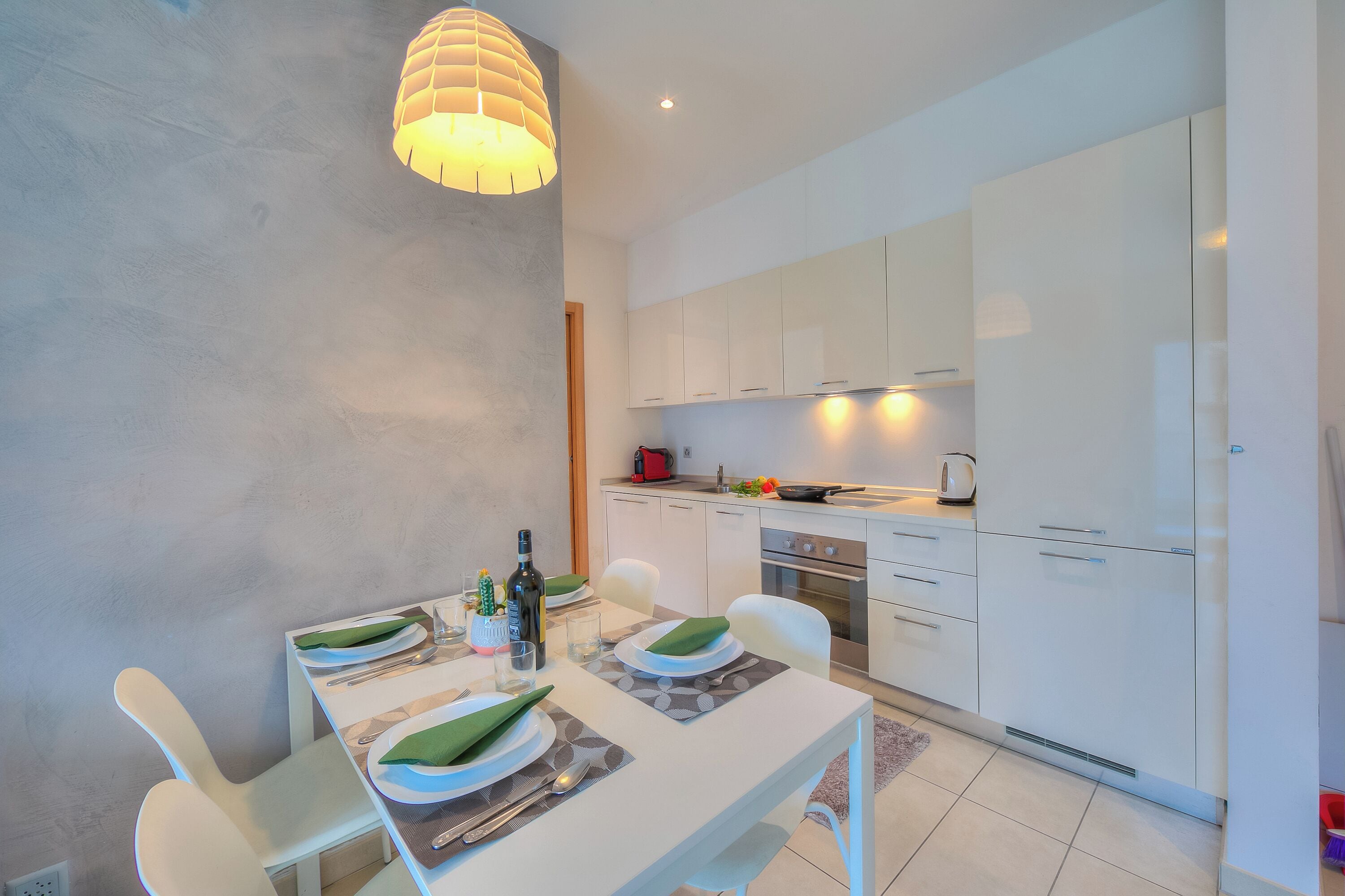 A modern kitchen with white cabinets, a dining table set for four, and a pendant light above.