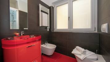 Un baño con tocador rojo, un bidé, un inodoro y una ventana con vidrio esmerilado.