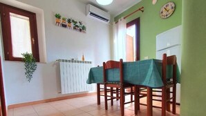 Un coin repas avec une table dressée pour quatre personnes, une plante suspendue, un appareil de climatisation et une horloge au mur.