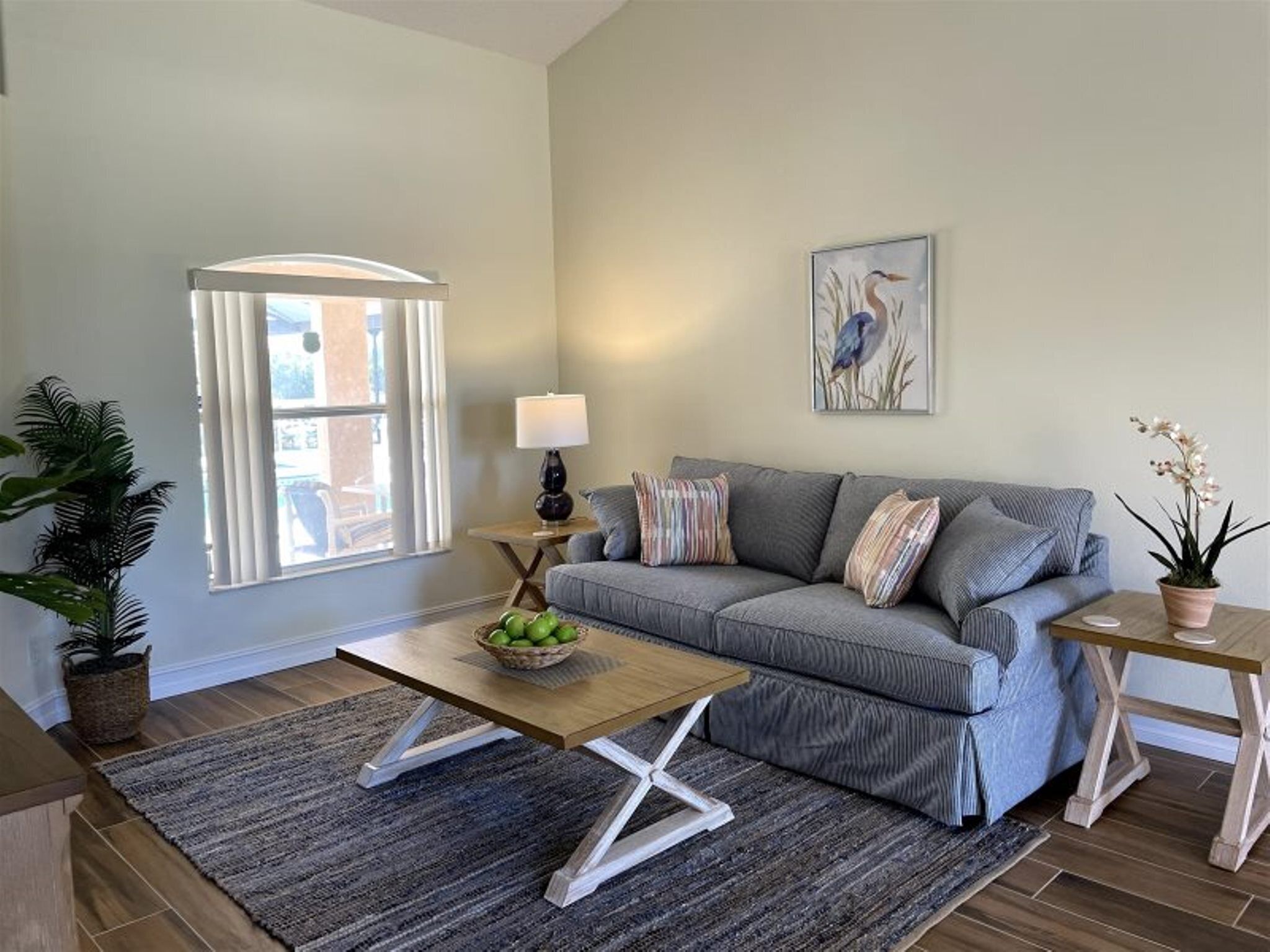 A living room with a grey sofa, a wooden coffee table, a lamp, a framed picture, and a potted plant.