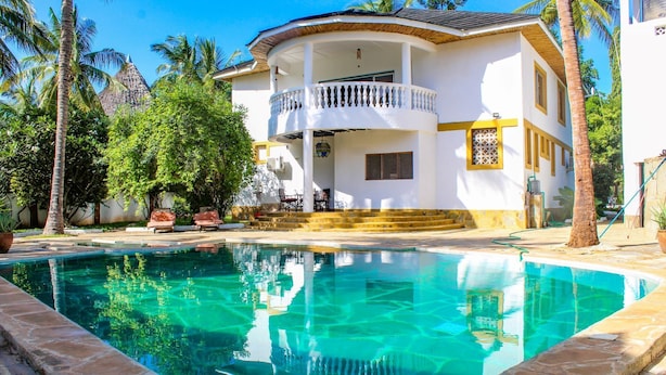 A two-story house with a swimming pool, surrounded by palm trees and a clear blue sky. - 5-bedroom Villa - 3 Mins Walk To The Beach (Diani Beach)