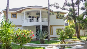 A two-story building with a balcony, surrounded by well-maintained gardens and palm trees. - 5-bedroom Villa - 3 Mins Walk To The Beach (Diani Beach)