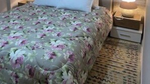 Una camera da letto con copriletto floreale, una testiera grigia, due comodini con lampade e un quadro con fiori appeso al muro.