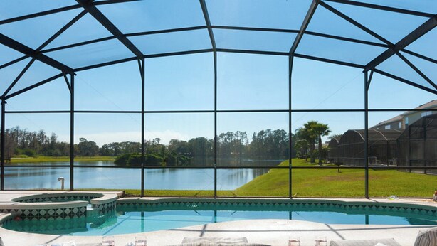 A pool area with a view of a lake, surrounded by a covered patio with seating and a table.