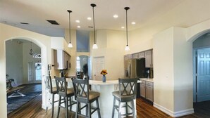 A modern kitchen with a central island, bar stools, pendant lighting, and a view into the dining area.